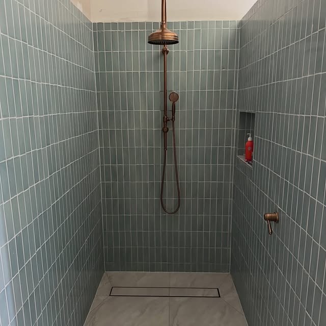 Finished shower lined in sage green tile with brass tapware and a linear drain